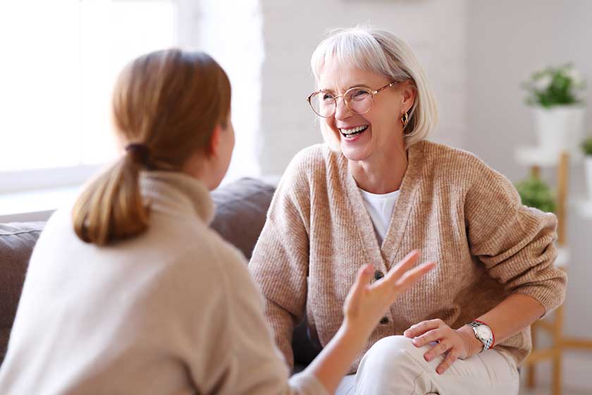 Adult and aged women laughing out loud at joke while relaxing on comfortable couch in cozy living room at home